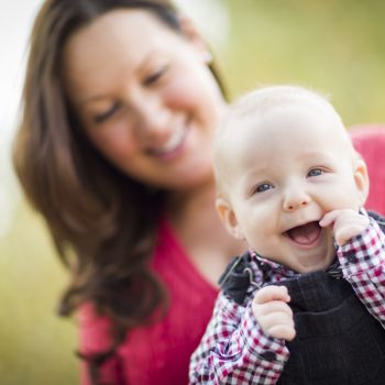Femme trentenaire portant un enfant a bout de bras, celui-ci étant particulièrement souriant, les deux sont vus de face.