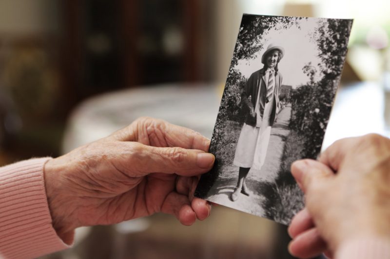 Détail d'une personne aux mains ridées et abimée tenant une très vielle photo en noir et blanc, d'elle meme