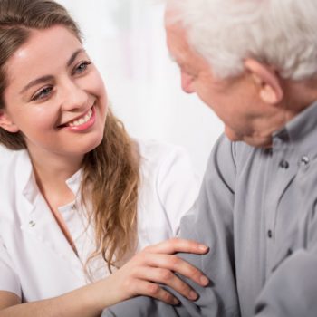 Vieil homme de profil parlant avec une infirmière vus de face, souriante.