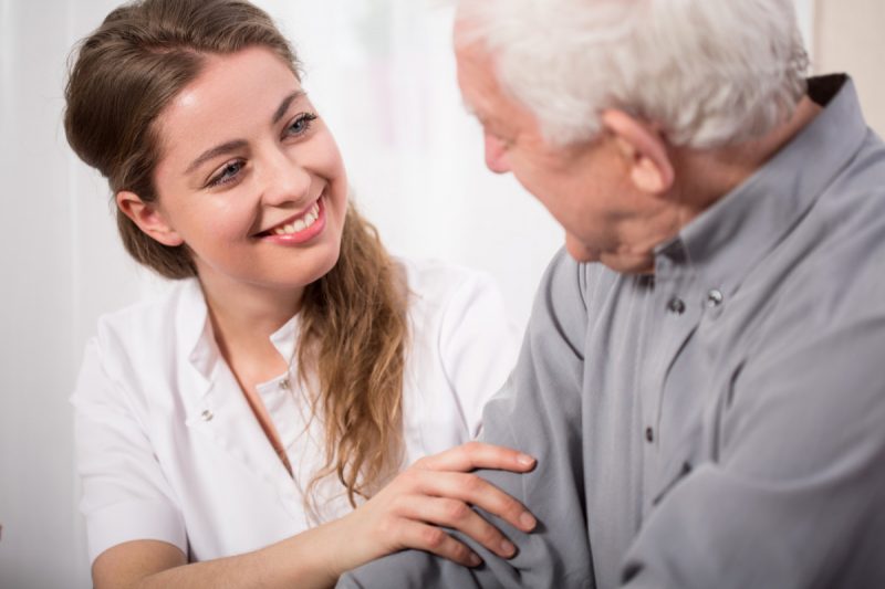 Vieil homme de profil parlant avec une infirmière vus de face, souriante.